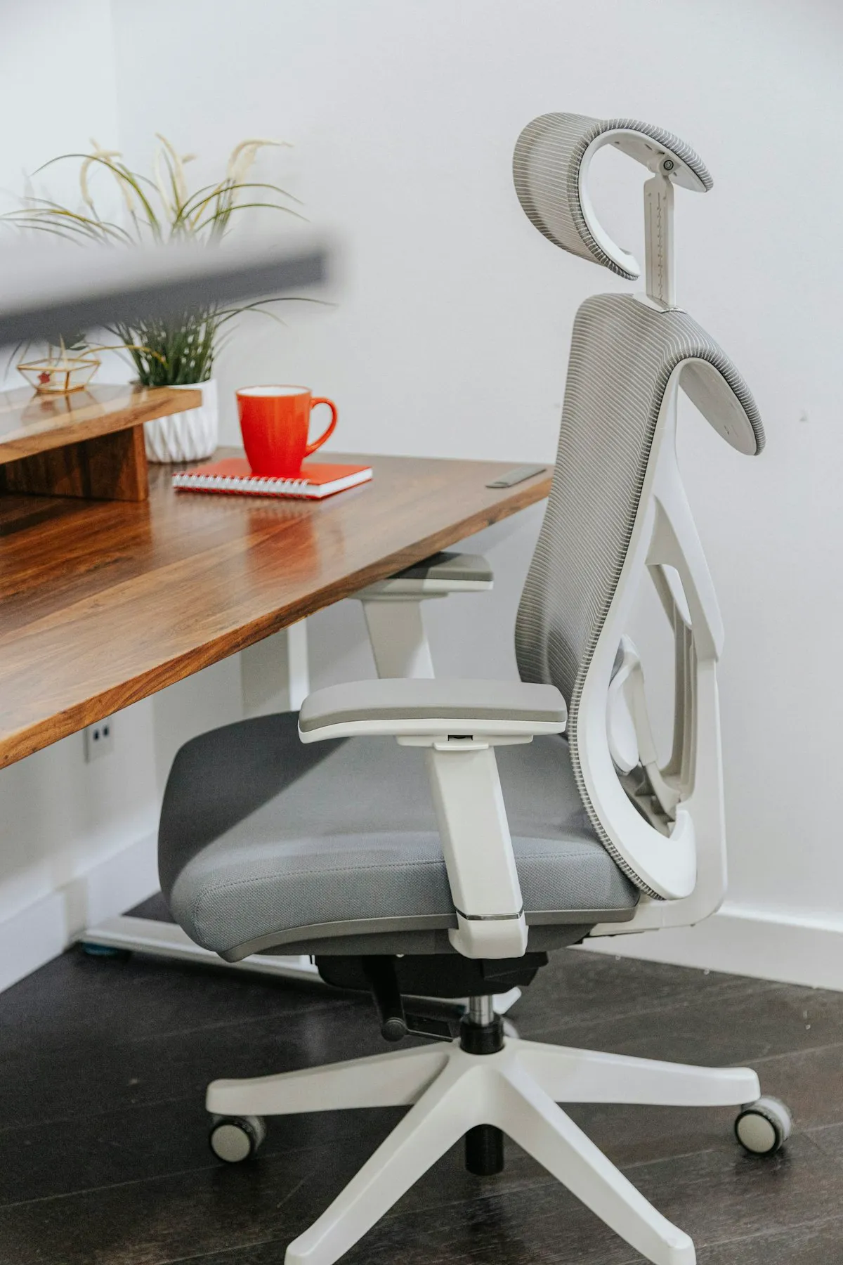 A grey ergonomic task chair with a headrest at a wooden desk
