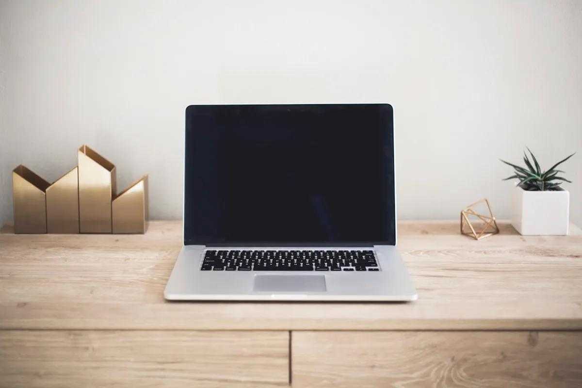 A laptop open on a wooden desk beside a plant