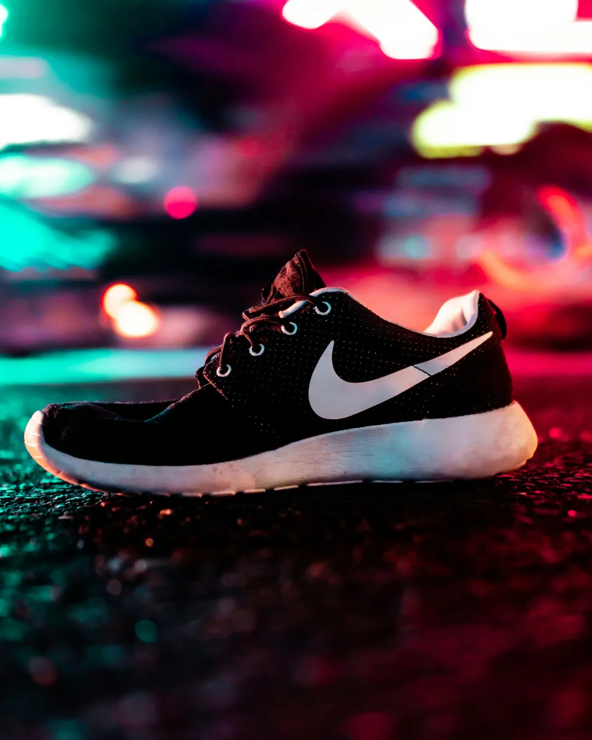 A black running shoe on a street lit by neon signs